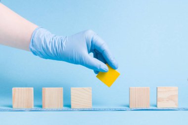 Tek kullanımlık lastik bir tıbbi eldiven al sarı bir blok tahta bir kare, domino taşları dizilmiş, mavi arka plan, kopya alanı, sosyal mesafe konsepti, hasta bir insanın toplumdan izole edilmesi.