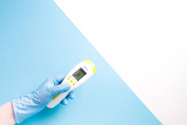 hand in a blue disposable rubber glove holds a high temperature infrared non-contact thermometer on a blue background, white background for text, copy space