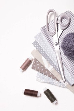 Beyaz arkaplanda desenli pastel kumaş gölgeleri, makas ve iplik makaraları, dikiş için gri yün örgü iplikleri ve aksesuarlar, kopyalama alanı, üst görünüm