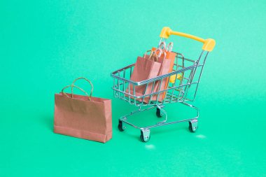 Yeşil arka planda minyatür bir alışveriş arabası, tramvayda küçük kağıt poşetler, fotokopi alanı, online alışveriş konsepti, bir çanta yakınlarda duruyor.
