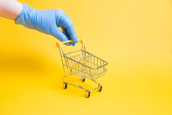 Een Hand Een Blauwe Wegwerphandschoen Houdt Een Miniatuur Winkelwagentje Bij — Stockfoto