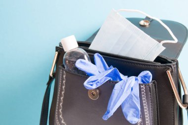 jel alkol dezenfektanı, yüz maskesi ve mavi plastik eldivenler mavi arka planda bir çantada, kopyalama alanı, salgın sırasında dışarı çıkarken ne alınır