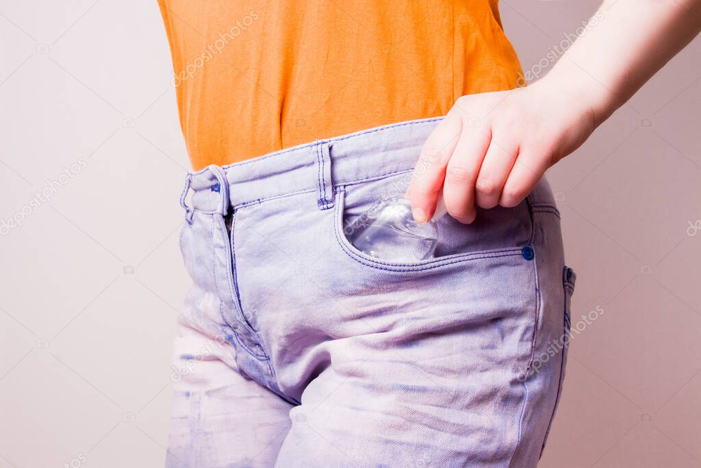 female hand puts a bottle of gel sanitizer in a pocket of blue jeans, copy space, light background