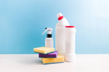Temizlik süngeri, etiketsiz beyaz şişeler deterjanlar ve masaya sprey, mavi arkaplan, kopyalama alanı