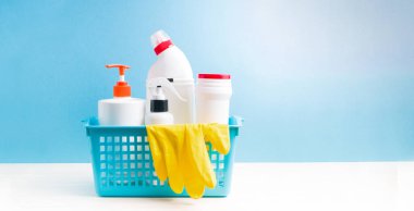 Mavi plastik bir kaptaki temizlik için sarı lastik eldivenler ve deterjanlar, mavi arkaplan, afiş, kopya alanı, etiketsiz beyaz şişeler