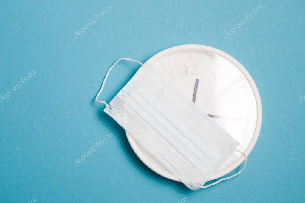 wall clock and medical face shield mask on a blue background