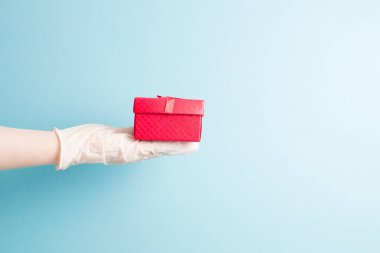 Mavi, tek kullanımlık bir eldivende kırmızı bir hediye kutusu vardır. Kırmızı bir kurdeleyle altın iplik, açık mavi arkaplan, kopyalama alanı.