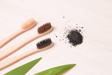 Tahta bir masada bambu diş fırçaları, bir demet kömür, yapraklar uzun bitkiler, çevre dostu yaşam tarzı konsepti.