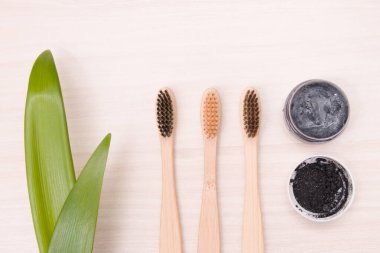 Bambu diş fırçaları ahşap bir masada doğal kaba kumaş üzerinde, ev yapımı kömür diş macunu küçük cam bir kavanozda, uzun bitkiler, eko dostu yaşam tarzı konsepti