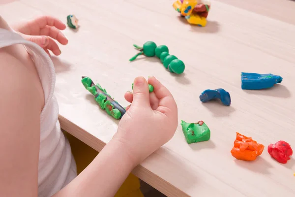 a small child sculpts from plasticine on a wooden table, the development of fine motor skills of hands, than to occupy a child at home, stay at home