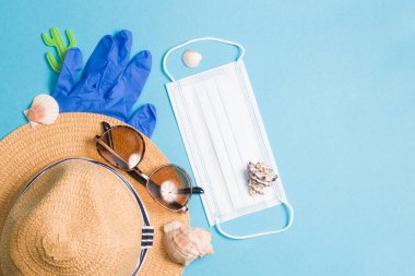 Tatil konsepti, hasır şapka, lastik eldiven, güneş gözlüğü, kabuk ve koruyucu yüz maskesi mavi arka planda, kopya alanı, üst manzara, karantina 2020