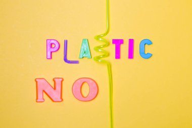 Plastik harfler ve atıklar yazılı. Plastik değil, şişe ve kokteyl tüplerinden bir şişe, sarı arka plan, fotokopi alanı, üst görünüm.