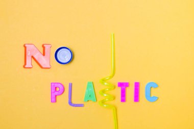 Plastik harfler ve atıklar yazılı. Plastik değil, şişe ve kokteyl tüplerinden bir şişe, sarı arka plan, fotokopi alanı, üst görünüm.