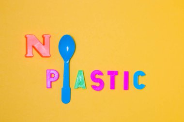 Plastik harflerden gelen yazıda plastik yok. O harfi ve L harfi yerine. Plastik mavi bir kaşık, sarı arkaplan, fotokopi alanı, üst görünüm.
