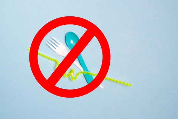 disposable plastic cutlery crossed out with stop sign of carcass color, blue background, top view, copy space, nature pollution concept