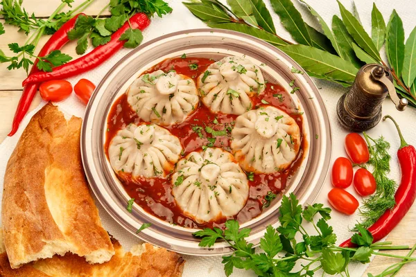 Georgian dumplings Khinkali with tomato spicy sauce on a plate among vegetables and greens