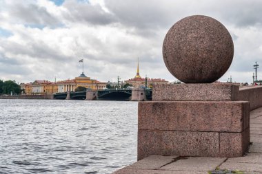 Strelka Vasilievsky adasının seddindeki granit top Neva nehrinin, Deniz Kuvvetleri binasının ve bulutlu St. Petersburg gökyüzünün arka planına karşı..