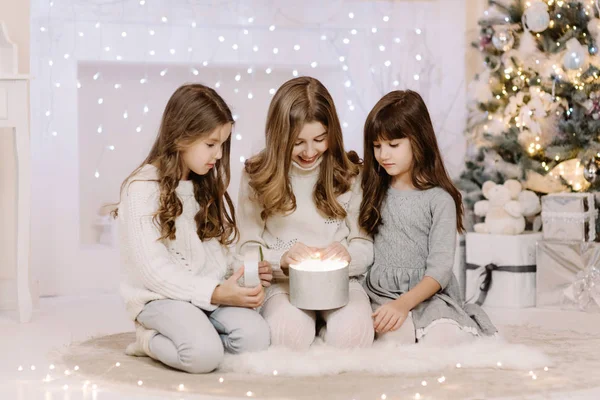 Happy three small sisters opening magical Christmas gift by fireplace in cozy bright living room on Christmas eve. Winter evening at home with family and kids. — Stock Photo, Image