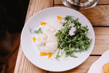 A Buratto ball and arugula raab salad on a plate. A delicious ball of Italian cheese.