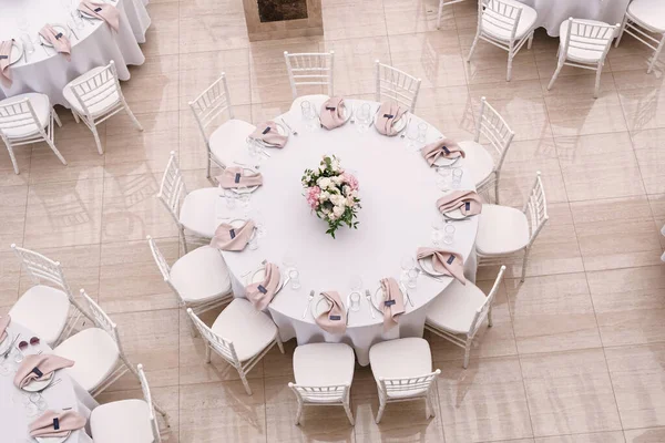 The luxurious round table for the wedding lunch is decorated with flowers and stylish dishes.