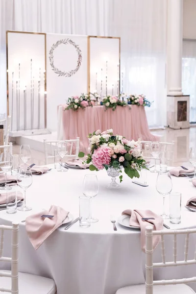 The luxurious round table for the wedding lunch is decorated with flowers and stylish dishes.