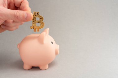 Bitcoin taşıma konsepti. Bitcoin 'ler için kumbara. Kripto para tasarrufu sembolü. Adamın biri para kutusuna gri arka planda bitcoin koyuyor. Boşluğu kopyala.
