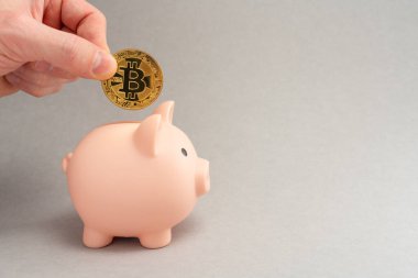 Bitcoin taşıma konsepti. Bitcoin 'ler için kumbara. Kripto para tasarrufu sembolü. Adamın biri para kutusuna gri arka planda bitcoin koyuyor. Boşluğu kopyala.