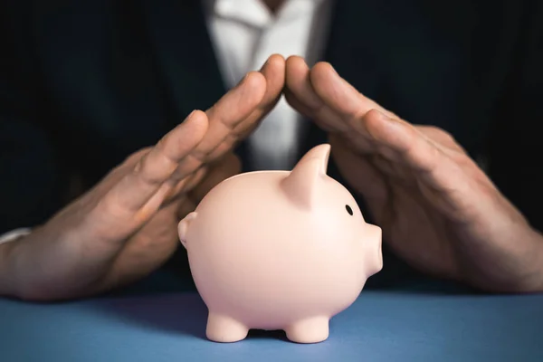 Money Protecting concept. Saving symbol - Close-up Of A Human Hand Protecting Pink Piggy Bank