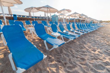 Güneş şezlongları ve saman şemsiyeli alçak mevsim boş plajlar. Girit şehrinde Hersonissos Günü fotoğrafı. Yunanistan tatili.