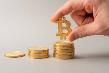 Bitcoin birikimi konsepti. Kripto para tasarrufu sembolü. Bir adam bozuk para yığınına para koyar, gri arka plan. Boşluğu kopyala.