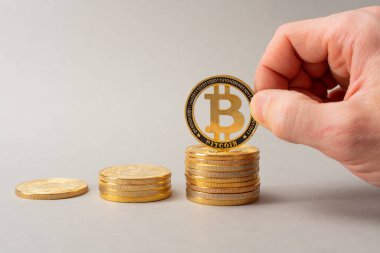 Bitcoin birikimi konsepti. Kripto para tasarrufu sembolü. Bir adam bozuk para yığınına para koyar, gri arka plan. Boşluğu kopyala.