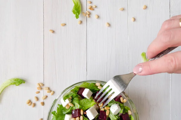 Salad of Beetroot, Feta cheese and lettuce leaves with pine nuts and fork in woman hand. Empty space — Stock Photo, Image