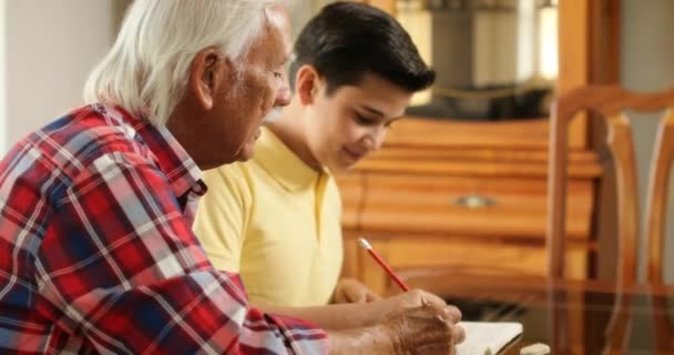 Senior Man helpen kleinzoon met School huiswerk thuis — Stockvideo