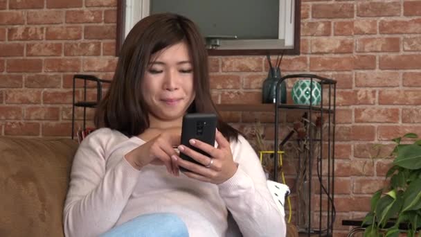 大学生のテキスト メッセージ携帯電話と笑顔します 自宅のソファーにアジアの女性 美しい日本の女の子は テキスト メッセージ インターネット メールにスマート フォンを使用します 技術を用いた楽しい幸せな人 — ストック動画