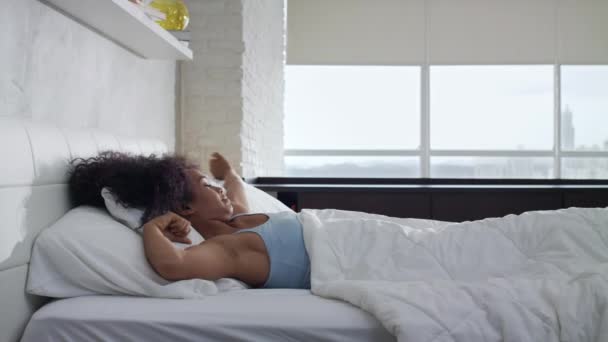 Красивая молодая афроамериканка просыпается в постели — стоковое видео
