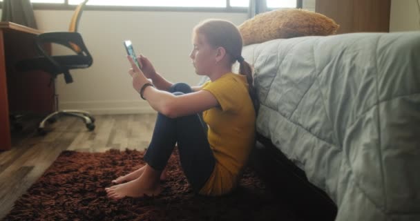 SMSka na mobilu za šikanování smutné holčičky v ložnici doma. Mladí lidé se dívají na mobil. Zrzavé dítě s emocemi, pocity smutku a osamělosti