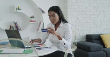 Siyahi bir kadın alışveriş sonrası kredi kartıyla ödeme yapıyor. Afrikalı Amerikalılar internet alışverişi için kart kullanıyorlar. Evde dizüstü bilgisayarı olan kız