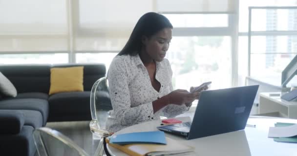 隔离期间在家里工作的黑人妇女 非裔美国人和流动工作 做远程工作 年轻的女商人带着手提电脑和手机工作 — 图库视频影像