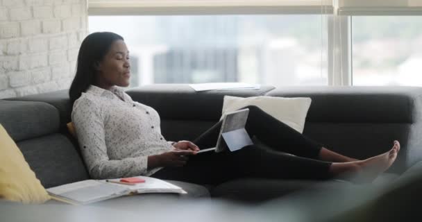 Porträt einer schwarzen Frau, die von zu Hause aus Meetings oder Webkonferenzen abhält. Afroamerikaner bei Fernarbeit. Junge Geschäftsfrau arbeitet mit Laptop, liegt auf Sofa
