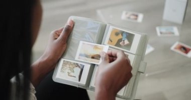 Siyah kadın evde taşınabilir kablosuz yazıcı ile resim basıyor. Afro-amerikan insanlar kanepeye oturup fotoğraf albümlerinde polaroid baskılar depoluyorlar. Omzundan vurulmuş.