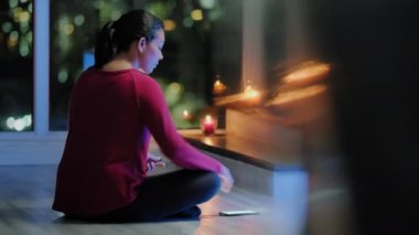 Gece evde yoga eğitimi alan bir kız. Genç İspanyol kadın akıllı telefonda uygulama yazılımı kullanarak meditasyon yapıyor. Sağlıklı bir yaşam tarzı ve meditasyon yapan insanlar.