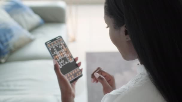 アフリカ系アメリカ人女性がスマートフォンで脳訓練のためにインターネットで遊ぶ オンラインゲームで携帯電話を使用している黒人 インターネットゲームで女性の肩のショットの上に — ストック動画
