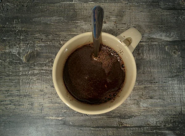 Eski ahşap yüzeyde bir fincan kahve fotoğrafın ortasında. Kaşık fincanda. Kupa seramikten yapılır..