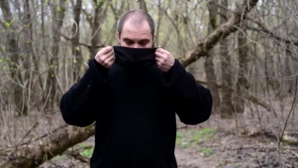 Egy férfi áll egy erdő mellett fekete orvosi maszkban a kovid-19 koronavírusból. — Stock videók