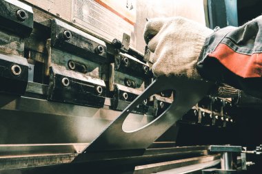 Eski bir makinedeki işçiler metali büker. Fabrikadaki eski bir makine. İşçi karanlıkta parçaları büker.