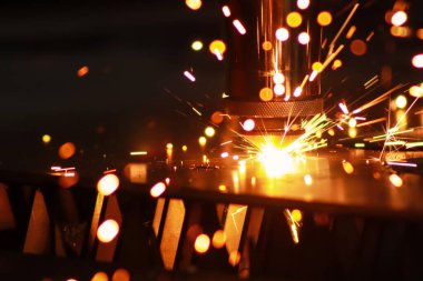 Lazer makinesi metal bir levhayı kesiyor ve parlak kıvılcımlar işlerinden uçup gidiyor. Metal fabrikasında lazer makinesi..