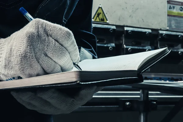 A worker makes notes in a notebook about the result of his work. A worker writes in a journal.