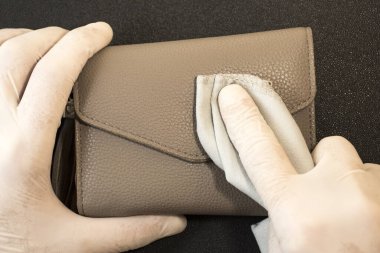 Tek kullanımlık eldivenlerdeki erkek elleri siyah arka plandaki bir cüzdandaki parmak izlerini siliyor. Eldivenli eller cüzdanı dezenfekte eder.