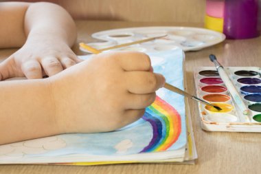 Bir çocuk suluboya ile bir gökkuşağı çizer. Bir çizim defterinde fırça ve boya ile bir gökkuşağı çizmek