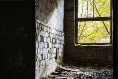 Eski, terk edilmiş, camları kırık, zeminde döküntüler ve duvarlardan fayanslar soyulmuş bir binanın odası.